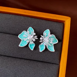 Dettaglio di orecchini a fiore in smalto turchese con zircone a cuore e mini perle