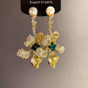 Detailed view of vintage-style gold earrings with emerald green gemstones and pearls