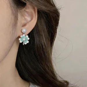 Dettaglio di orecchini a fiore in smalto verde menta con perle indossati da una modella