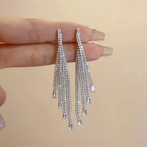 Macro detail of elegant silver-plated zircon tassel earrings held by manicured fingers