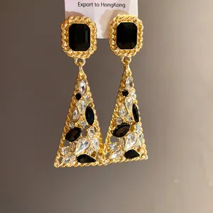Macro detail of vintage gold-tone triangle drop earrings with black and clear stones