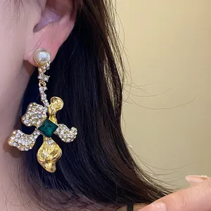 Close-up of vintage gold dangle earring with emerald green gemstone and rhinestones