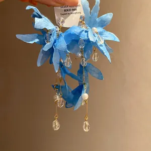 Macro detail shot of elegant blue fabric flower earrings with pearls and crystal tassels.