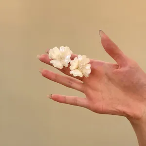 Primo piano di eleganti orecchini a fiore bianco con petali cristallini scintillanti su una mano