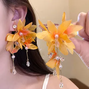 Close-up detail of vibrant orange fabric flower earrings featuring pearls and long tassels