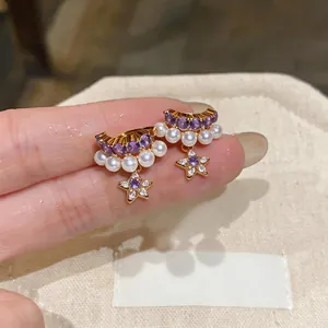 Close-up of elegant star pearl clip-on earrings with purple zircon and gold finish.
