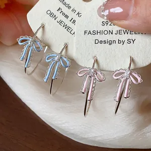 Close-up of delicate enamel ribbon bow earrings with silver hoops and zircon stones.
