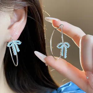 Close-up of elegant silver hoop earrings with blue enamel bow and zircon detail