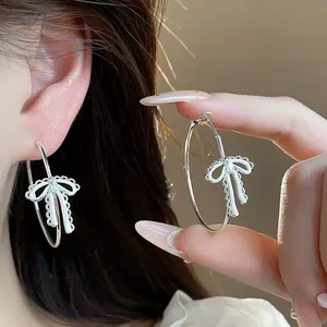 Detail showing silver hoop earrings with white enamel lace bow charms and sparkling zircon