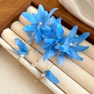 Macro detail of blue fabric flower earrings with pearls and gold tassels in a display box