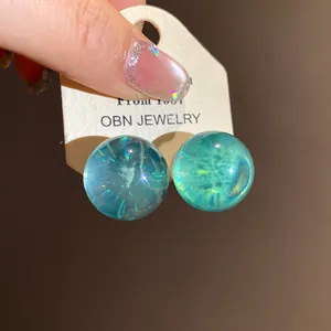Detailed macro view of blue-green resin stud earrings with a shimmering galaxy inner effect