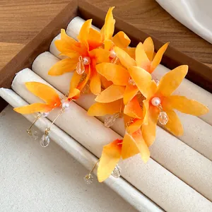 Close-up of elegant orange fabric flower earrings featuring pearl and clear crystal tassels