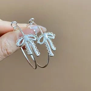 Macro detail of silver hoop earrings featuring white enamel bowknots and zircon.