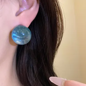 Macro detail of a round translucent blue resin stud earring on a female ear model