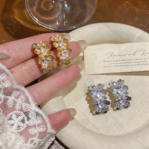 Primer plano de elegantes pendientes de flores con circonitas en acabados oro y plata