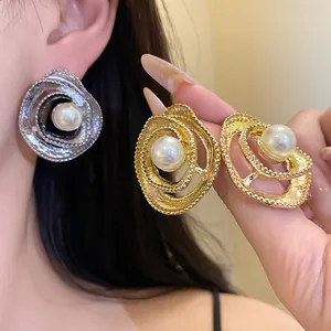 Close-up of elegant textured metal spiral earrings with central faux pearl on model