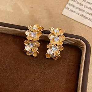 Primer plano de pendientes dorados con forma de flor y centros de circonita.
