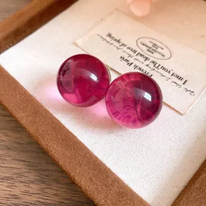 Close-up of translucent magenta resin ball stud earrings on a textured background