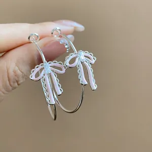 Close-up of silver hoop earrings featuring pink enamel bow and a sparkling zircon