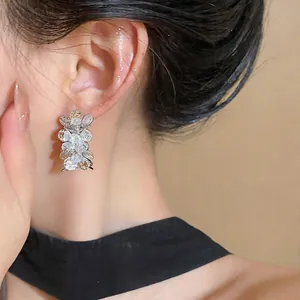 Primer plano de pendientes florales plateados con circonitas brillantes en la oreja.