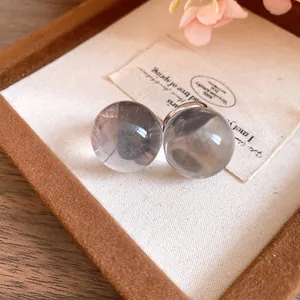 Detailed close-up of minimalist grey resin sphere stud earrings in a wooden jewelry box
