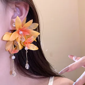 Close-up of elegant fabric flower earrings with pearls and long tassels.