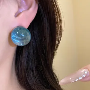 Close-up of a blue round resin earring with a shimmering galaxy effect on the ear.