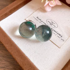 Detailed view of minimalist translucent green resin round stud earrings in a wooden jewelry box