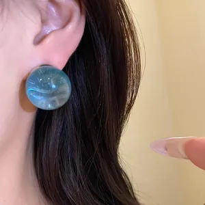 Close-up detail of a minimalist blue translucent resin round stud earring worn on an ear