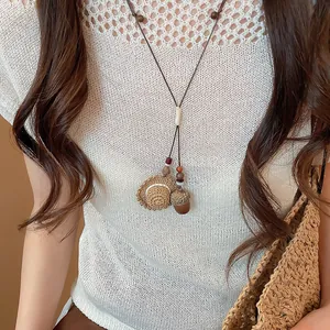 Close-up of a Mori style necklace with straw hat and acorn charms on a white top