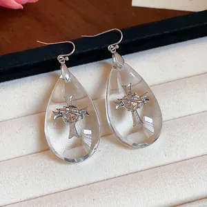 Dettaglio di orecchini a goccia in acrilico con croce di strass incorporata.