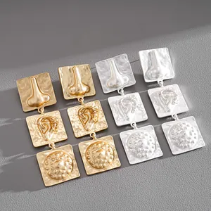 Detail view of exaggerated square earrings featuring unique nose and ear relief patterns.