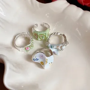 Ensemble de quatre bagues à fleurs colorées sur plateau coquillage blanc, design esthétique