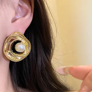 Close-up view of vintage gold textured spiral stud earrings with a central white pearl.