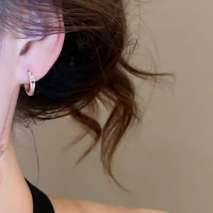 Detailed close-up of an elegant silver hoop earring with blue zircon on model ear