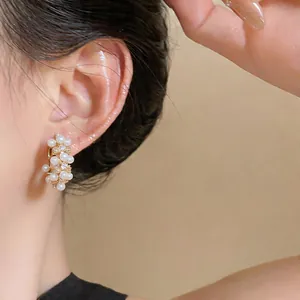 Close-up of elegant gold hoop earrings with white pearls and zircons on model's ear