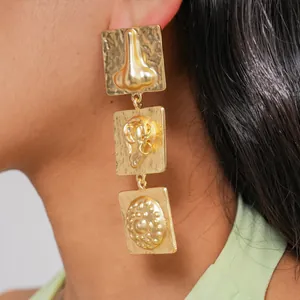 Detail shot of unique gold square drop earrings featuring anatomical nose and ear motifs