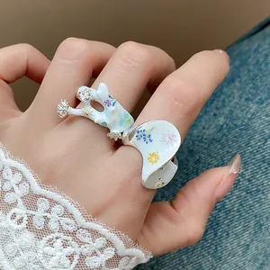 Gros plan d'une bague fleur en émail blanc avec imprimés floraux colorés et strass