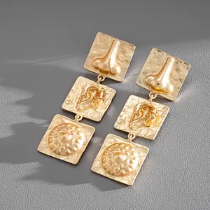 Detailed view of gold-tone tiered square earrings featuring unique anatomical relief patterns.