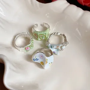 Gros plan de quatre bagues à fleurs en émail coloré dans un plat en forme de coquillage