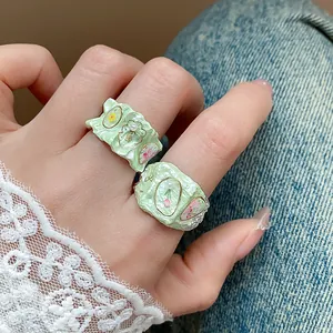 Détail de bagues en émail vert clair avec des motifs floraux et des perles sur un modèle.