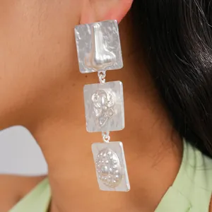 Close-up detail of silver geometric earrings with embossed abstract facial features