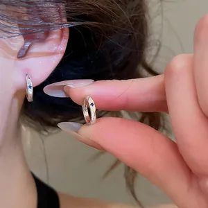 Close-up of minimalist silver hoop earring with small blue zircon stone held by fingers