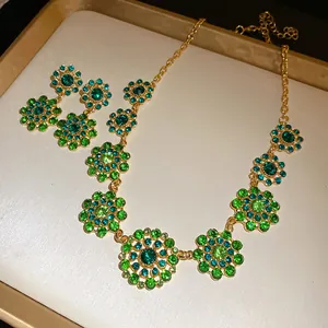 Close-up detail of gold-tone necklace and earrings with green rhinestone flower patterns