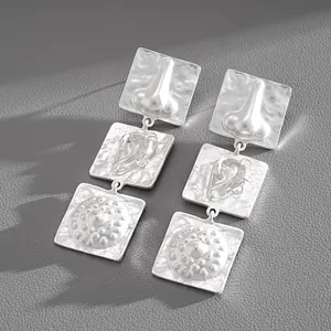 Close-up of avant-garde silver square drop earrings with 3D anatomical relief patterns