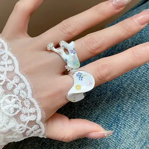 Gros plan détaillé de bagues en émail fleuri portées sur une main avec dentelle chic.