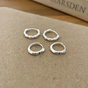 Macro detail of silver hoop earrings with blue zircon and scalloped texture designs.
