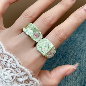Gros plan de bagues fleurs en émail vert menthe avec perles sur une manche en dentelle.