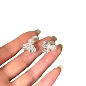 Hand holding a pair of elegant silver bow knot earrings with white round pearls