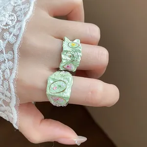 Vue détaillée de bagues fleurs vert menthe avec des motifs floraux en émail sur un doigt.